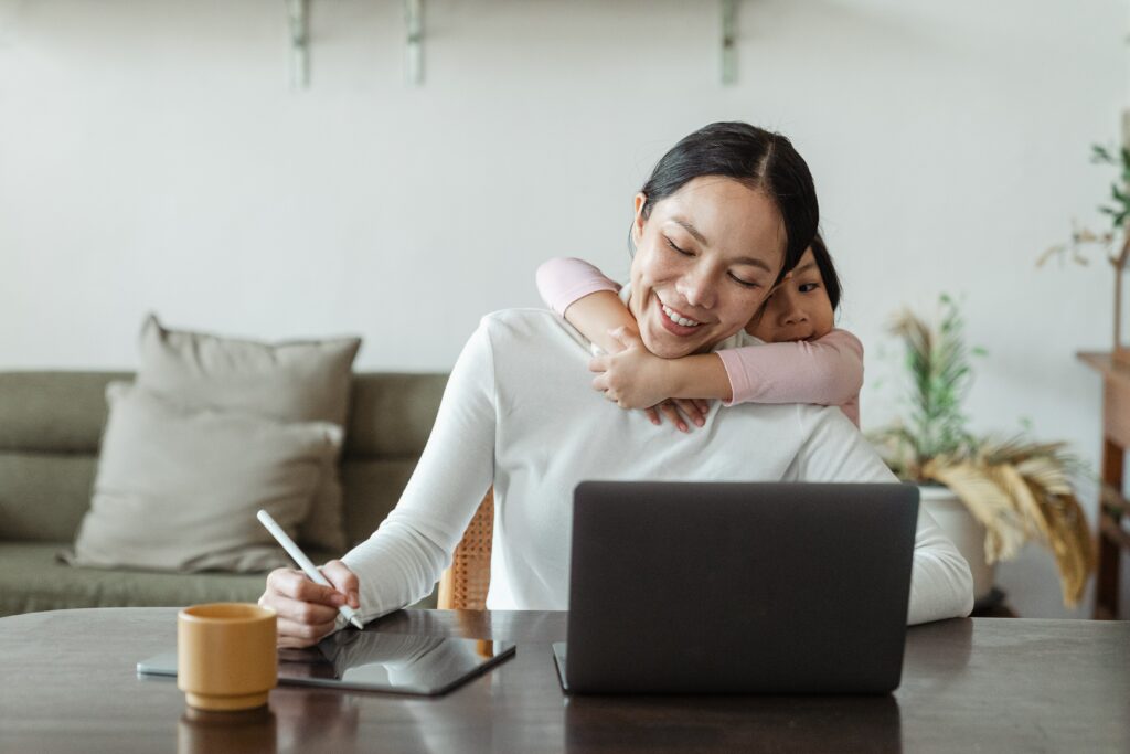 Image of a person, working from home while hugging a child.