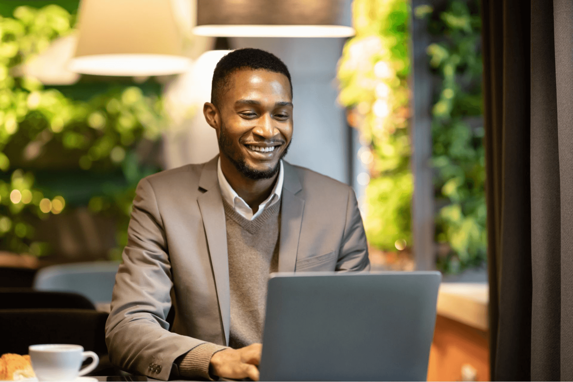 A professional man in a suit, with a cheerful expression, is working on his laptop.